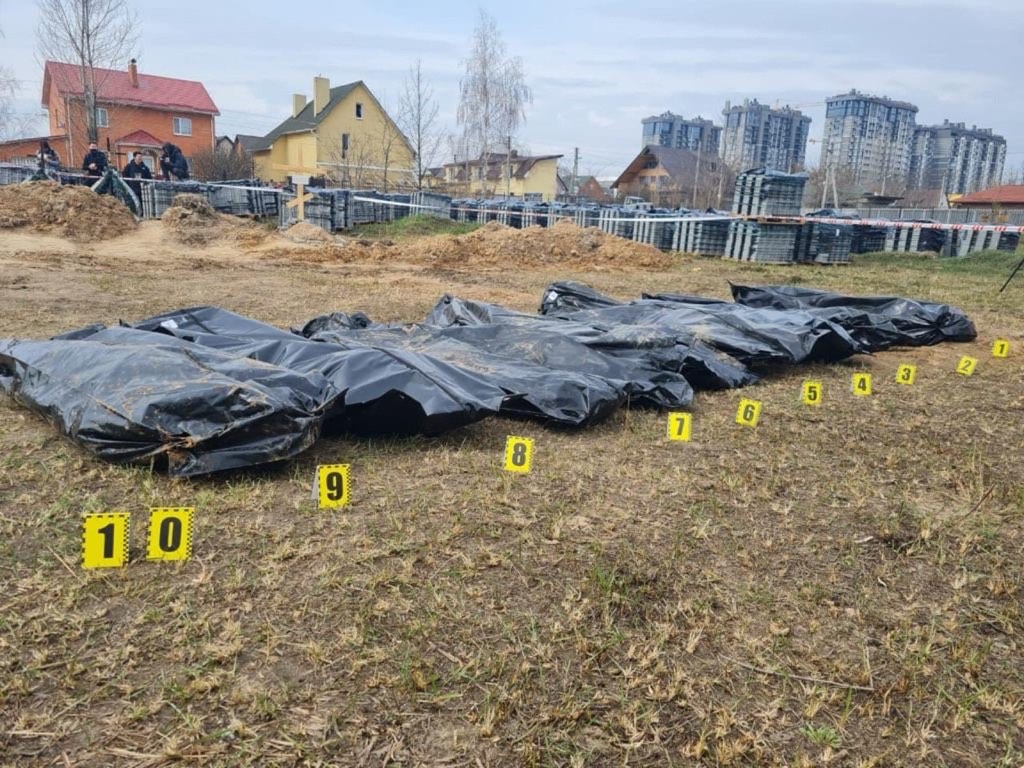Exhumation site in Bucha, Ukraine, with numbered forensic markers beside body bags recovered from a mass grave.